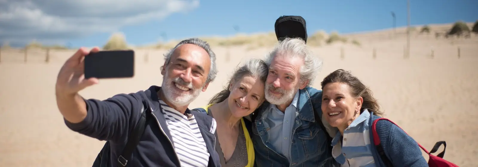 Four smiling friends taking a selfie together on a sandy beach.